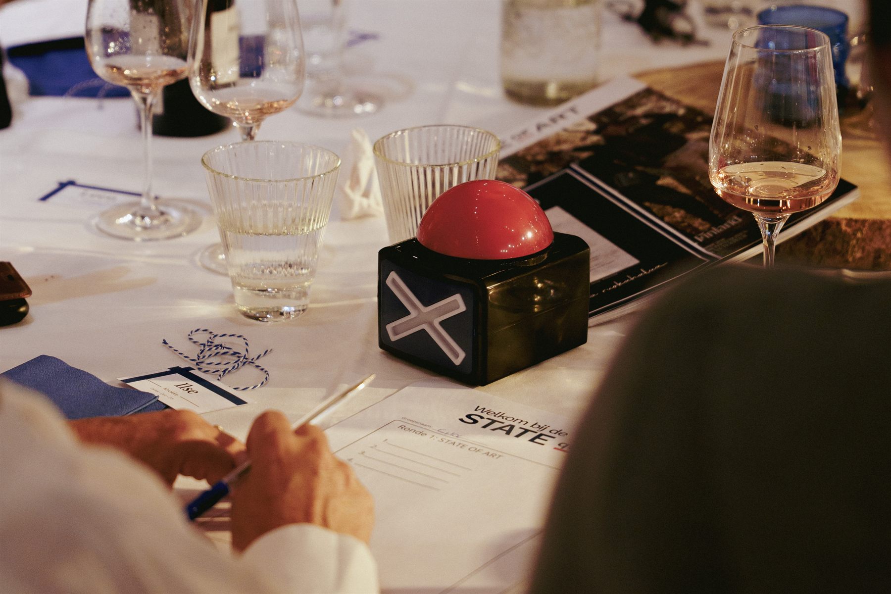 Tafel met een rode buzzer, quizbladen en wijnglazen